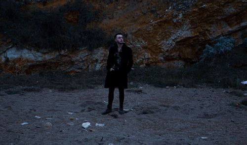 Full length of young man smoking cigarette while standing at beach against mountain