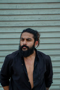 Bearded man looking away while standing against wall