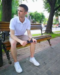 Full length of young man sitting on bench in park