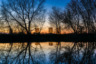 Silhouette bare trees by lake against sky during sunset