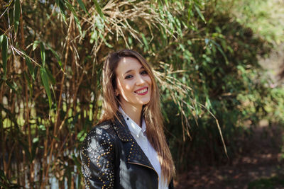 Portrait of smiling young woman standing against trees in park