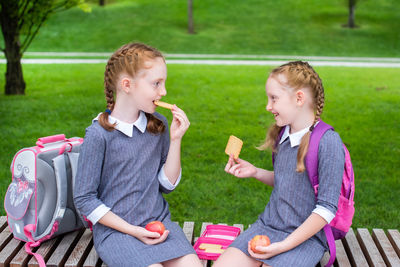 Smiling friends eating food while sitting on grass outdoors