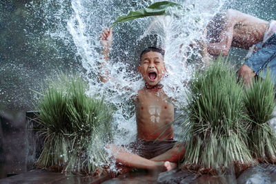 Laughing boy sitting in water by plant