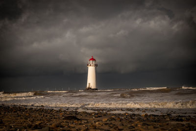 Lighthouse by sea against sky during sunset