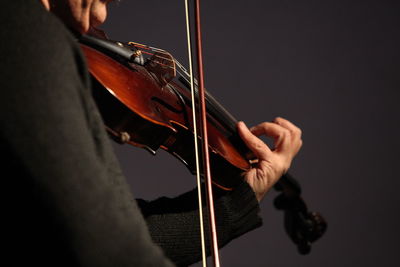 Midsection of man playing violin against gray background