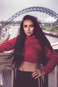 Portrait of beautiful young woman standing against bridge in city