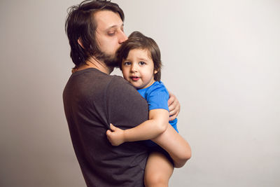 Father in the gray shirt holding a son in a blue t-shirt in the hands of a white wall