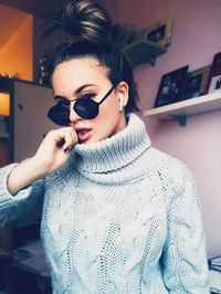 Portrait of fashionable teenage girl wearing sunglasses and sweater standing at home