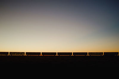 Silhouette freight train against clear sky during sunset