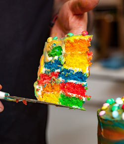 Person holding a slice of a rainbow colorful cake.