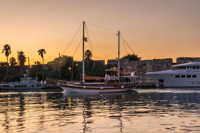 Boats moored in harbor at sunset