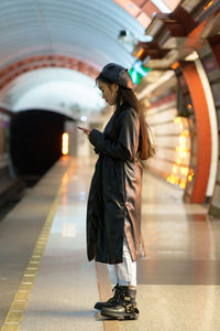 Trendy asian girl wait for train at subway platform check email or online schedule in smartphone