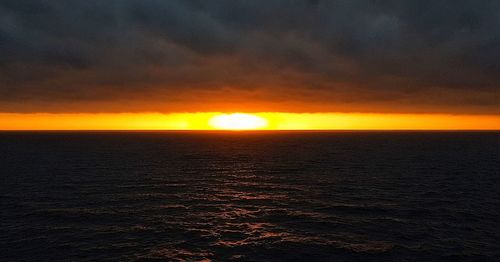 Scenic view of sea against dramatic sky during sunset