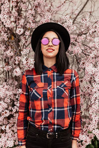 Portrait of woman wearing sunglasses standing against cherry blossom