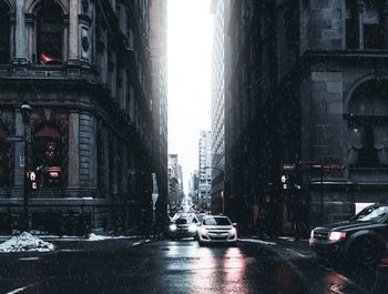 Cars on street amidst buildings during rainy season