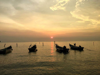 Silhouette people on sea against sky during sunset