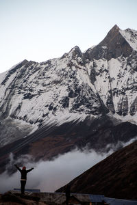 Rear view of woman with arms outstretched standing by snowcapped mountain