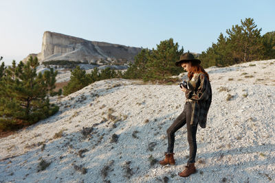 Portrait of young woman standing on rock against sky