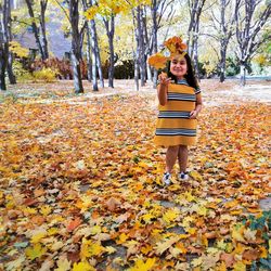 Portrait of young woman standing by leaves during autumn