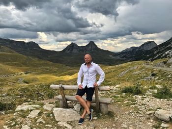 Full length of man sitting on bench against mountain