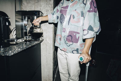 Midsection of young man with crutch making coffee at workplace