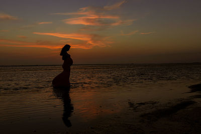 Silhouette woman on beach against sky during sunset