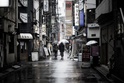 People walking on wet street amidst buildings in city