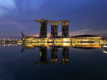 Illuminated built structure by lake against sky at night