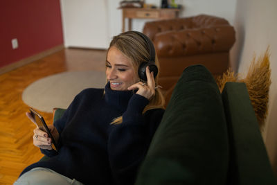 Woman listens to music with headphones lying down on her couch  mobile phone, urban living.