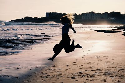 Full length of woman on beach against sky during sunset