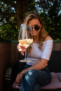 Portrait of woman wearing sunglasses holding drink while sitting on chair