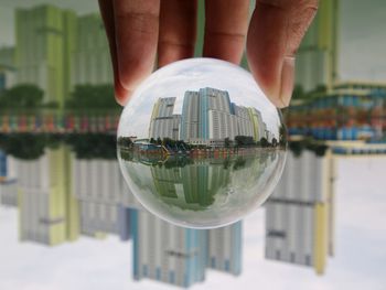 Midsection of person holding crystal ball with reflection of cityscape