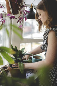 Young woman repots a plant and works her hands into the soil