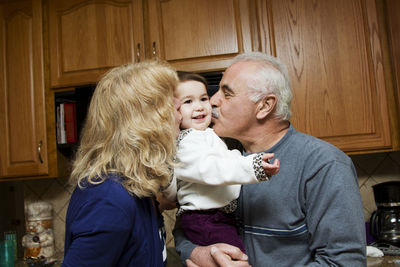 Grandparents kissing child while standing in kitchen