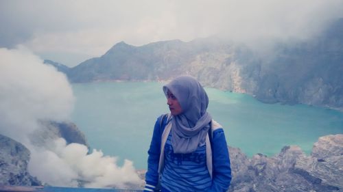 Woman wearing hijab sanding on mountain against lake