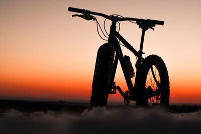 Silhouette bicycle parked against sky during sunset