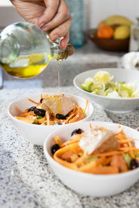 Close up of hand pouring olive oil over a salad with olives and