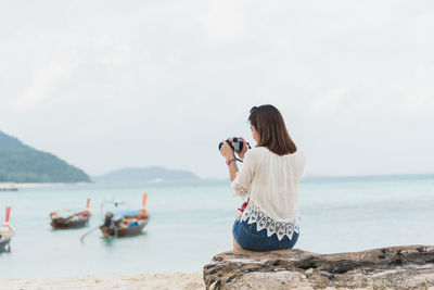 Woman photographing at beach against sky