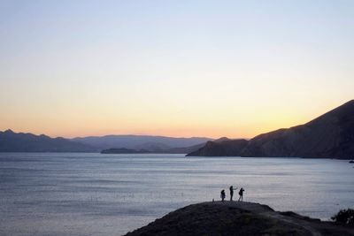 3 young girls on shore of the sea against sky during sunset