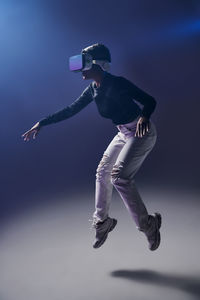 Full body female in modern vr headset jumping above ground on dark background in studio while exploring virtual reality in