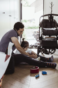 Father talking on smart phone while tying baby son's shoelace at home