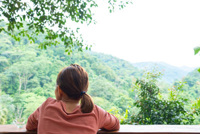 Rear view of woman sitting against trees