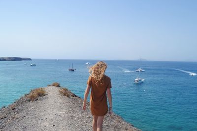 Rear view of woman walking at beach against clear sky