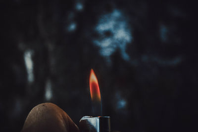 Close-up of human hand holding burning cigarette lighter at dusk