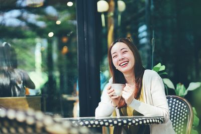 Portrait of smiling young woman using mobile phone while sitting at park