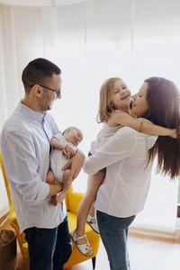 Family of four with newborn baby holding by dad. mom kissing older sister