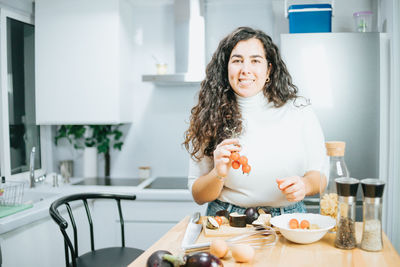 Portrait of smiling woman holding food in kitchen