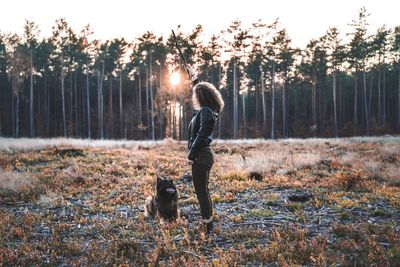 Woman holding stick with dog on field against sky