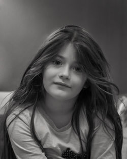 Close-up portrait of girl smiling while sitting against wall