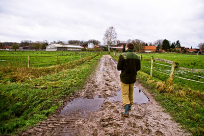 Rear view of man walking on agricultural field against sky
